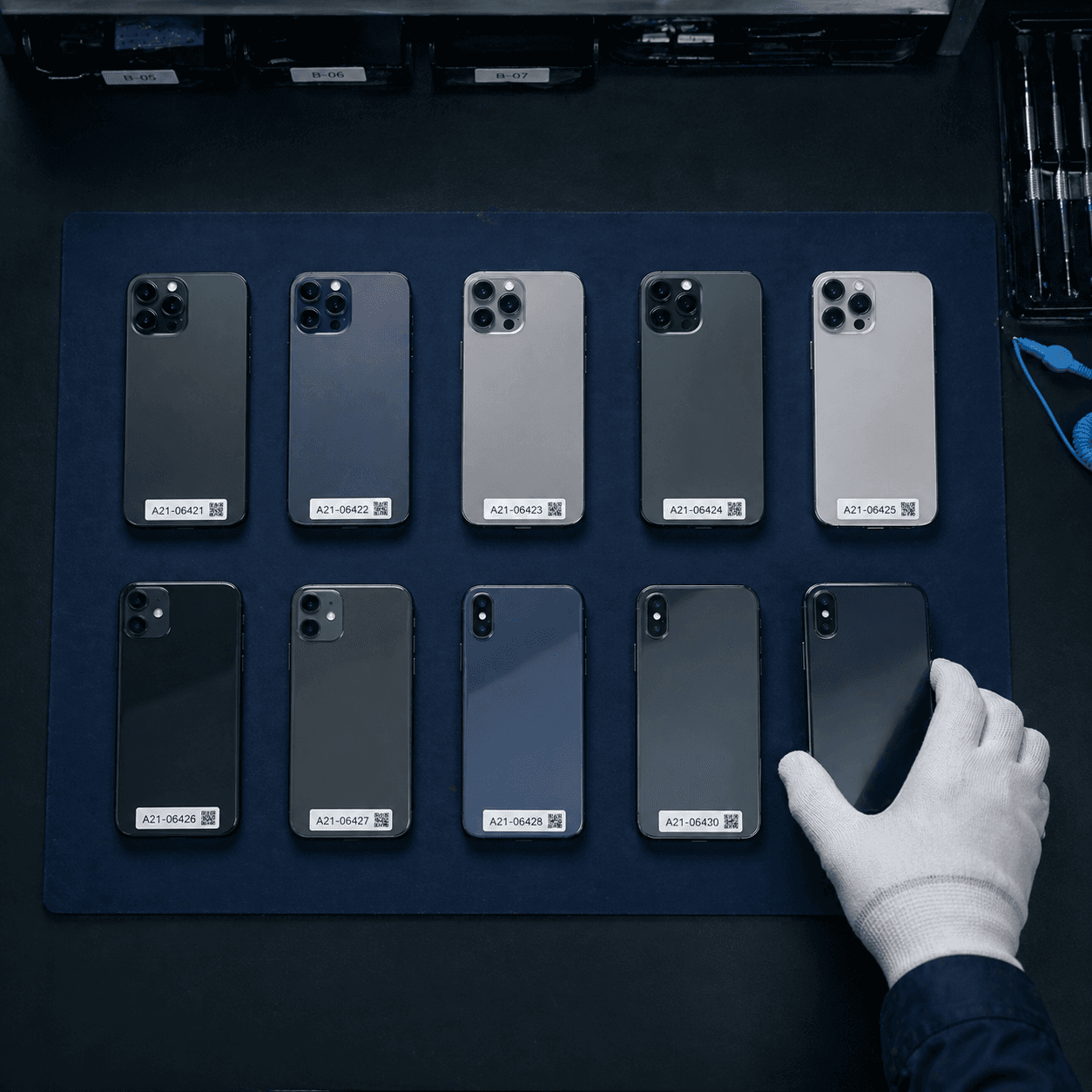 A grid of refurbished smartphones laid out on a navy ESD mat