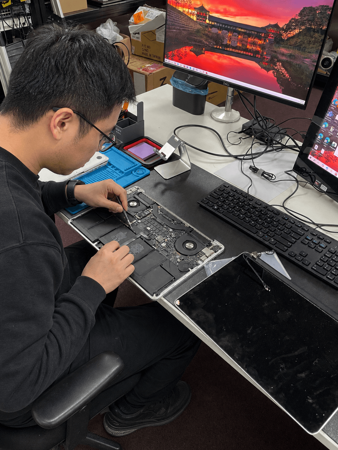 A technician inspecting a MacBook Pro logic board with precision tweezers at the workbench